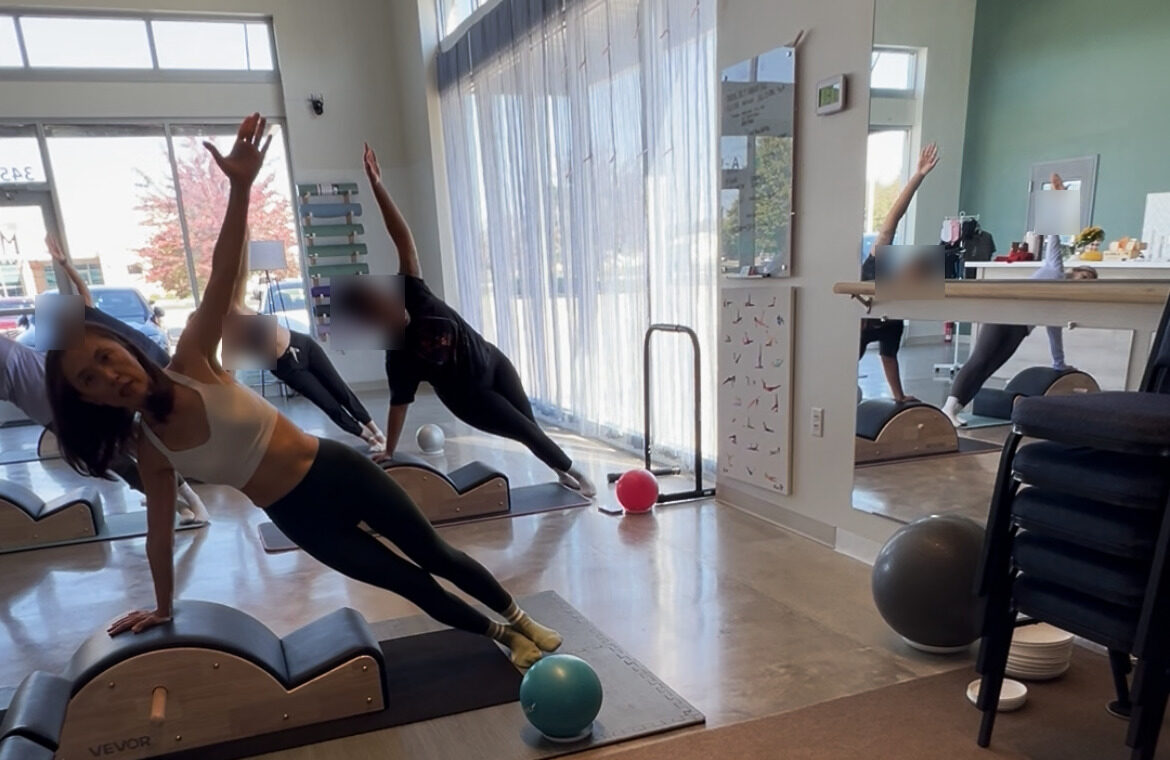 Euna leading a side plank on the spine corrector with the class behind her (client faces blurred)