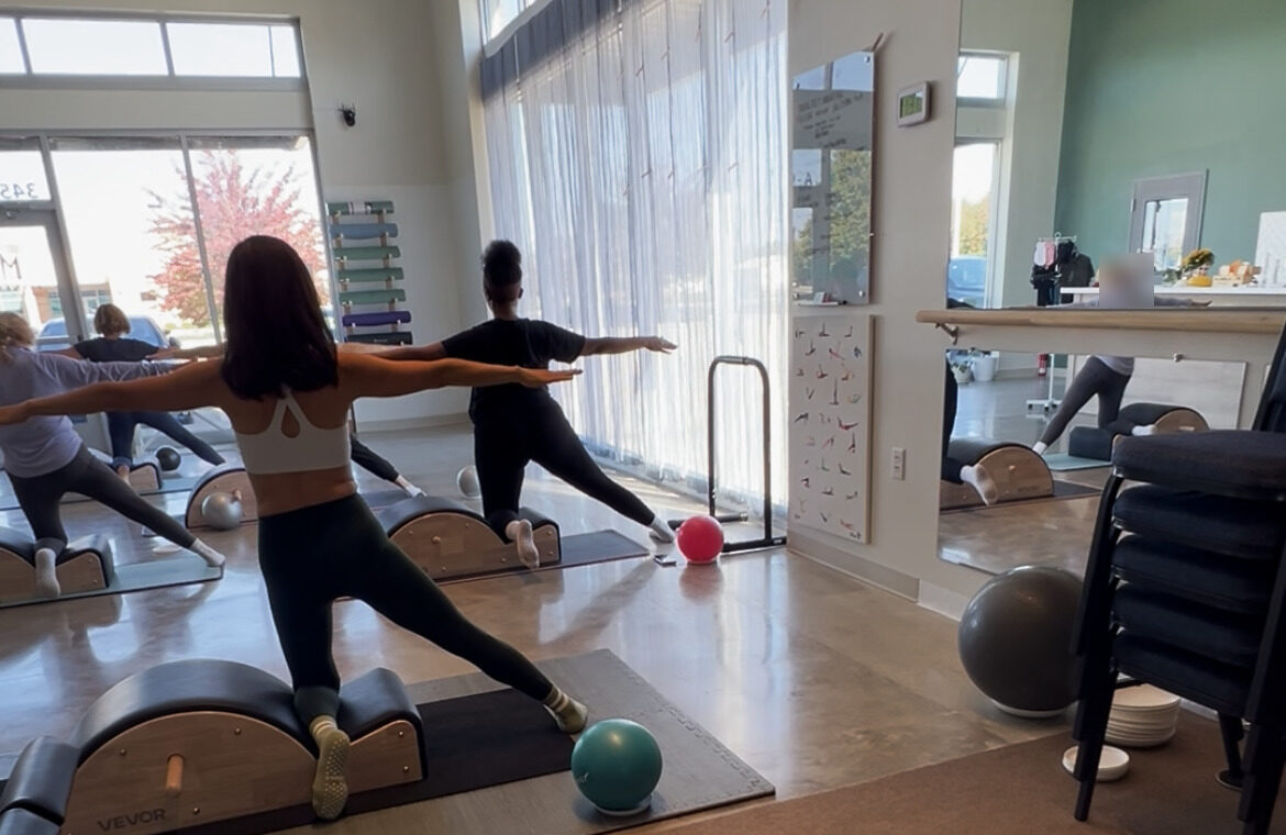 Euna and the class in a lunge with arms out beside their spine correctors (client faces blurred)