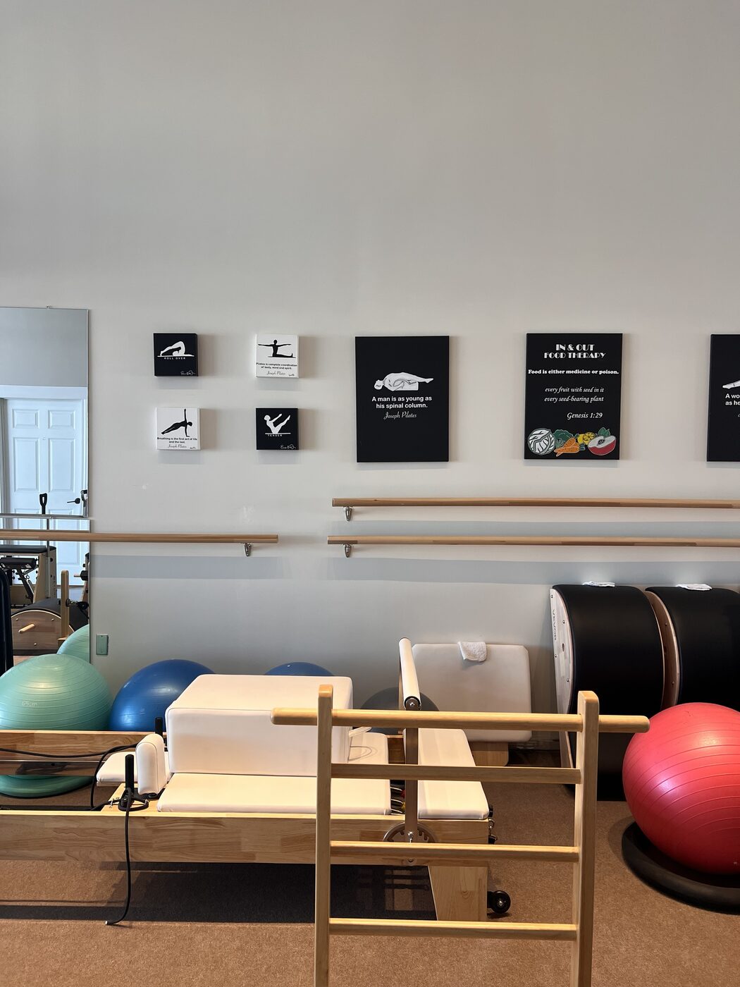 The machine room at the new studio: a reformer and wall chair under framed Joseph Pilates quotes and the In & Out Food Therapy sign