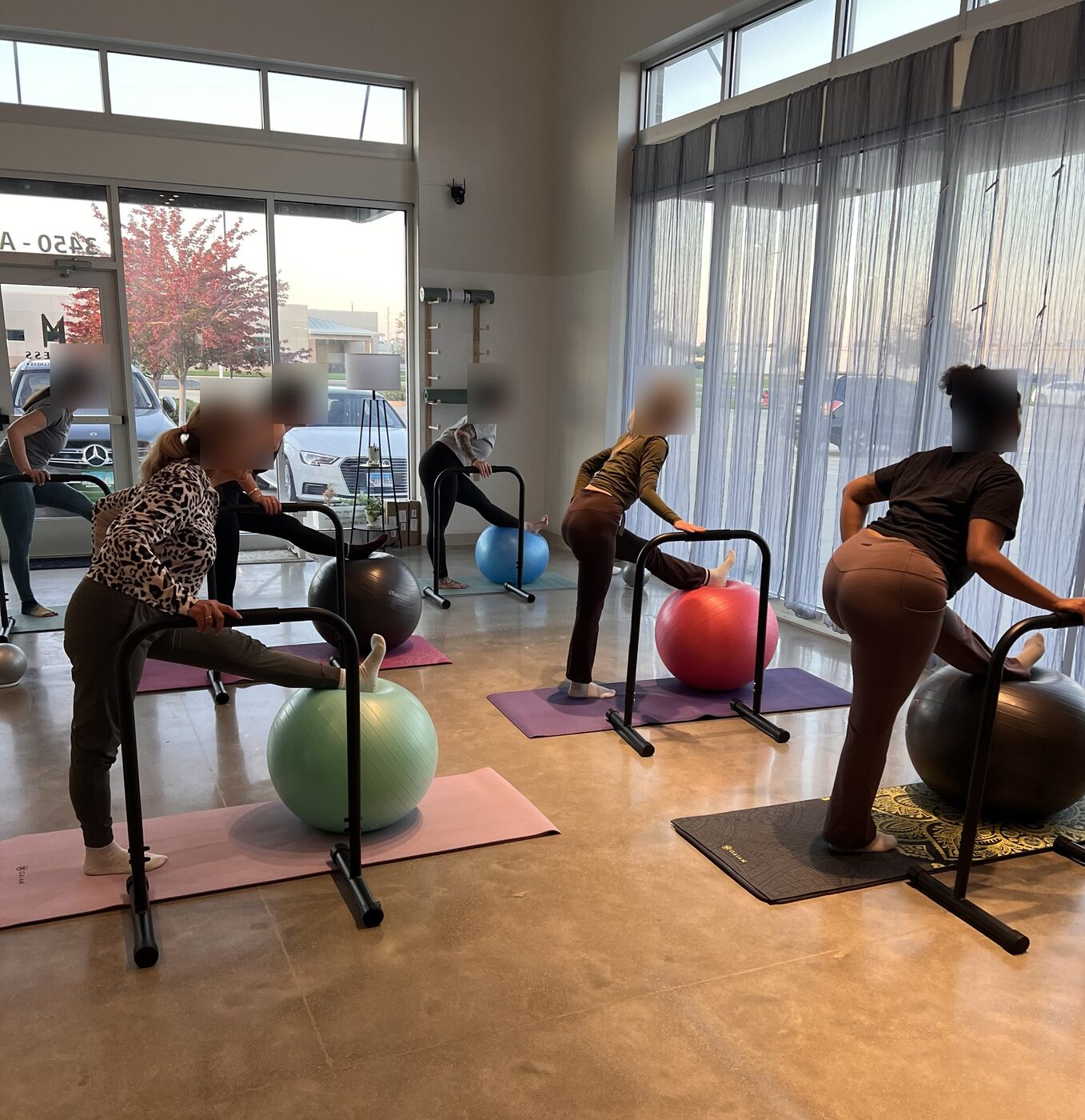 An MBB class at the new IN & OUT Pilates studio: clients at the bars with one leg on exercise balls along the front windows (client faces blurred)