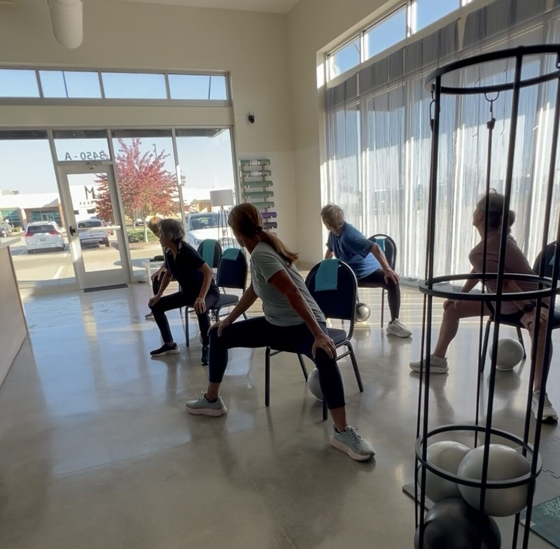 A Silver Powerhouse chair Pilates class twisting through the shoulders in the sunny front room of the new studio