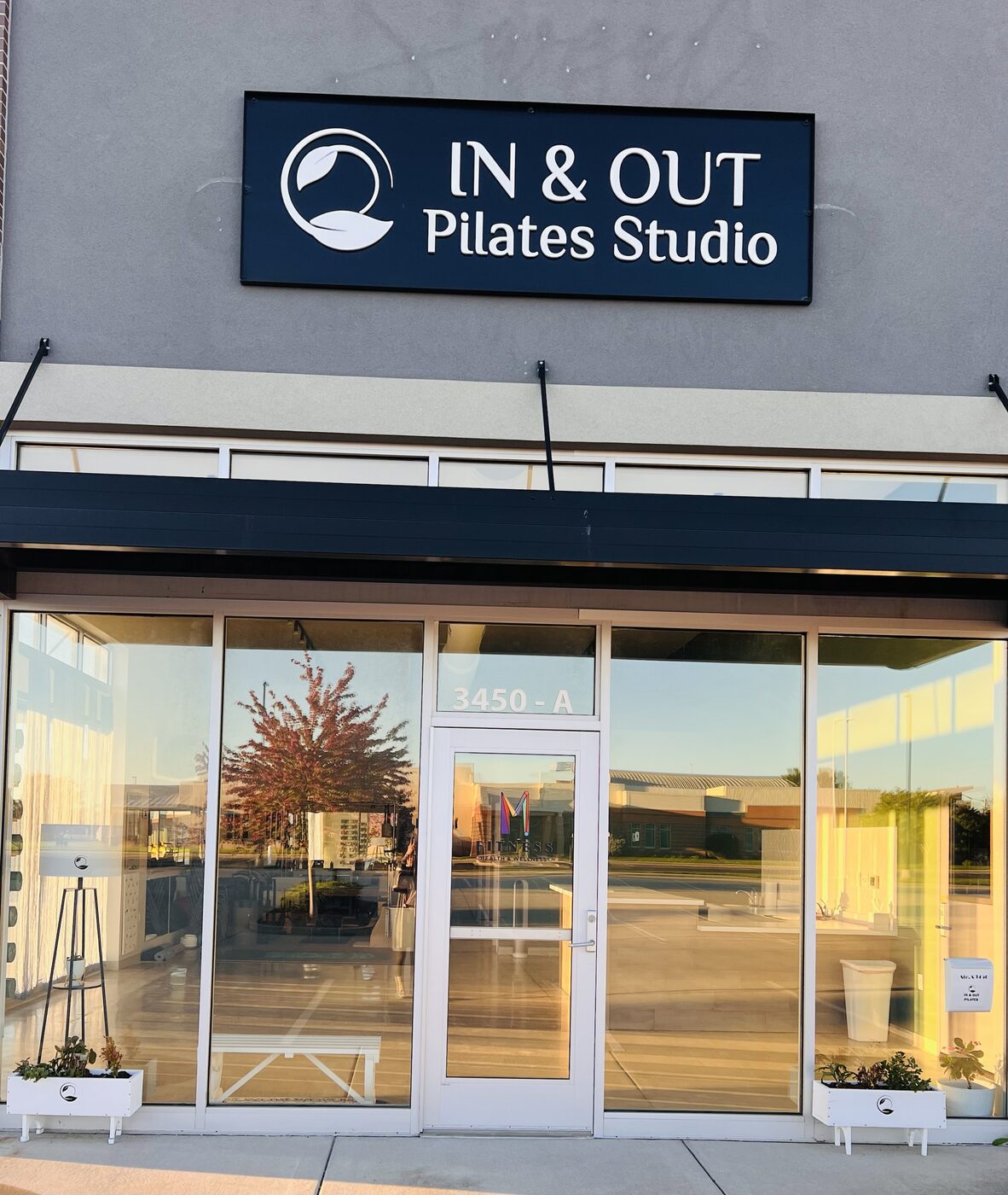 The studio's front door under the IN & OUT Pilates Studio sign, with white planter boxes on each side